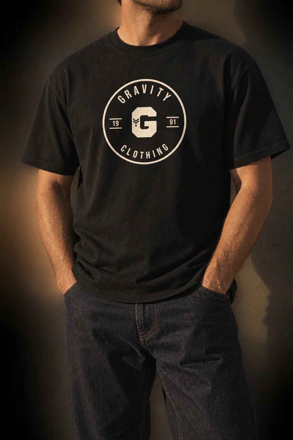 Man wearing the black Gravity Clothing varsity badge tee against a concrete wall in warm evening light